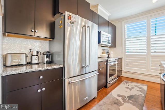 kitchen with appliances with stainless steel finishes, tasteful backsplash, light wood-type flooring, and light stone counters