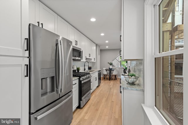 kitchen with appliances with stainless steel finishes, recessed lighting, backsplash, white cabinets, and light wood-style flooring