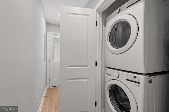 washroom featuring estacked washer and dryer, light wood-style floors, and baseboards