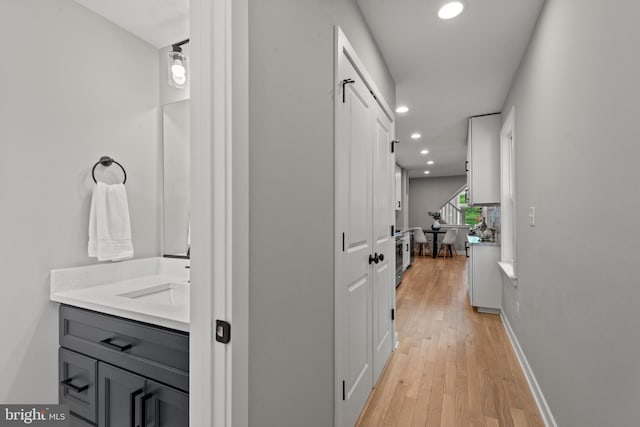 hallway featuring recessed lighting, light wood finished floors, and a sink