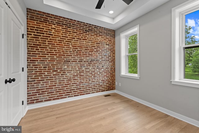 unfurnished room with brick wall, baseboards, a ceiling fan, plenty of natural light, and light wood finished floors
