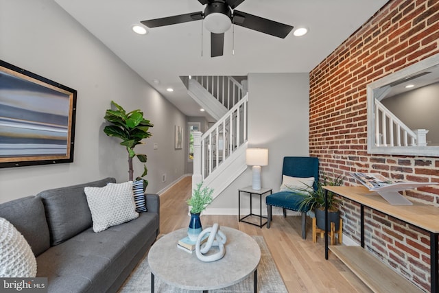 living room with wood finished floors, stairs, ceiling fan, brick wall, and baseboards