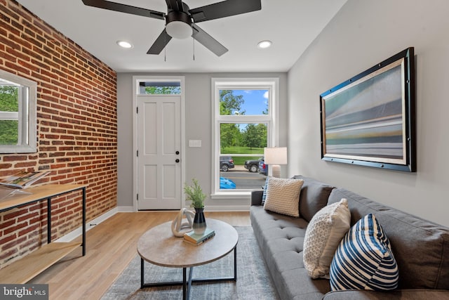 living area with brick wall, plenty of natural light, light wood-type flooring, baseboards, and recessed lighting