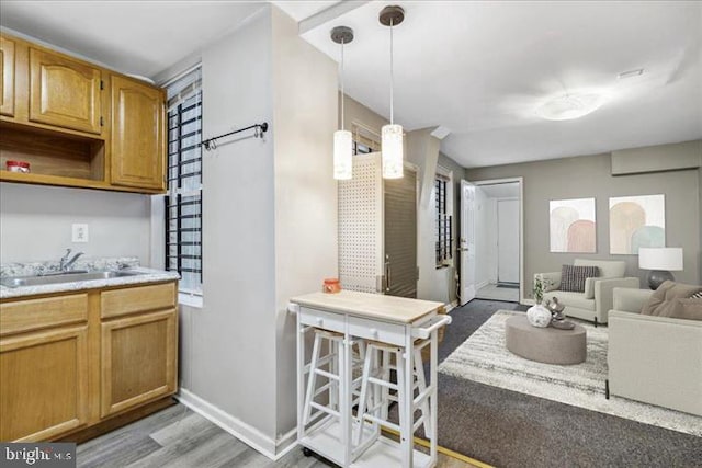 kitchen with a sink, light countertops, baseboards, light wood-style flooring, and pendant lighting