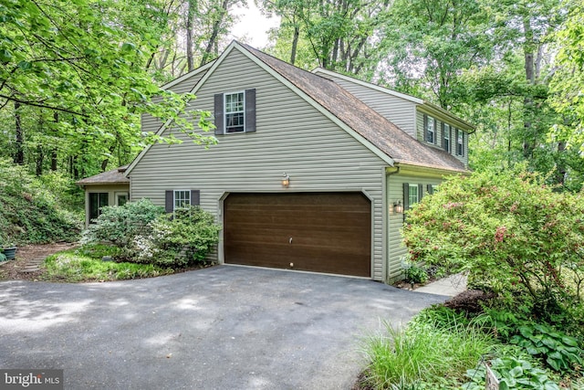 view of side of home featuring driveway, a garage, and roof with shingles