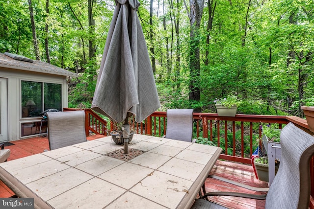 wooden terrace featuring outdoor dining area and a wooded view