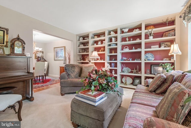 carpeted living area featuring baseboards, a chandelier, and built in shelves
