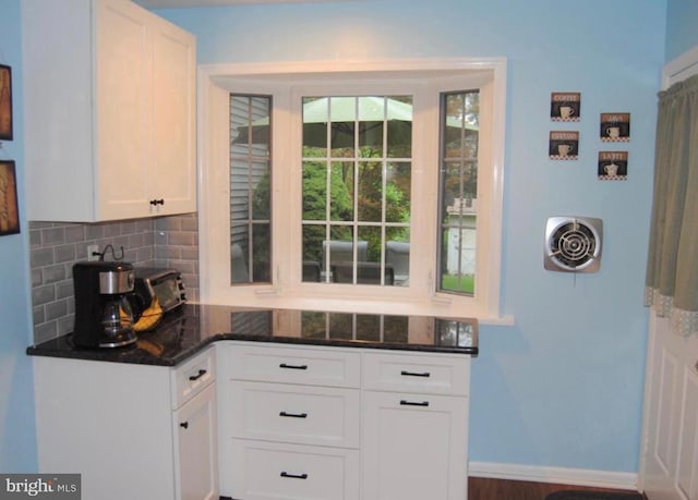 kitchen with backsplash, white cabinets, dark stone counters, and baseboards
