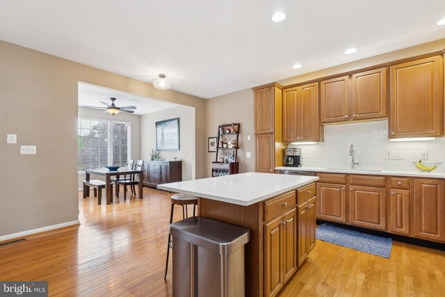 22615 Upperville Heights Sq, Ashburn, VA 20148 - kitchen featuring a sink, light countertops, light wood-style flooring, decorative backsplash, and brown cabinets