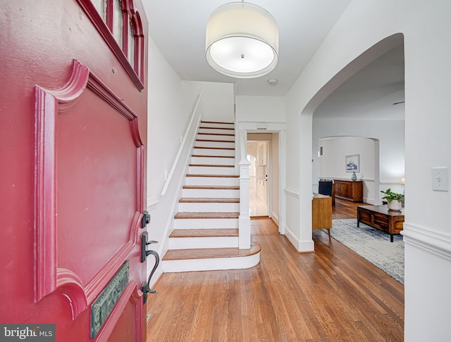 entryway with arched walkways, wood finished floors, and stairway
