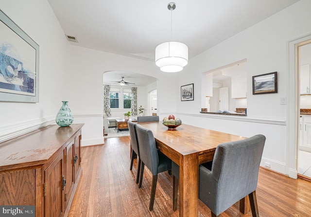 dining area featuring arched walkways, light wood-style floors, and ceiling fan