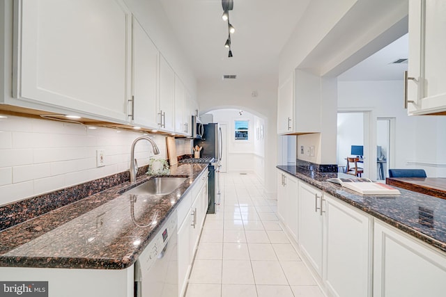 kitchen with a sink, stainless steel appliances, arched walkways, white cabinets, and light tile patterned flooring