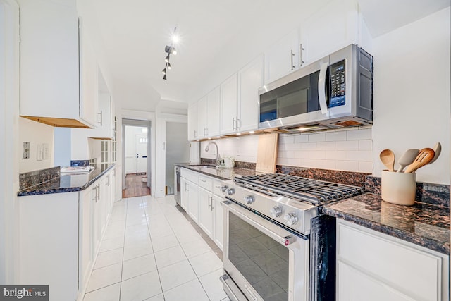kitchen with stainless steel appliances, a sink, white cabinets, light tile patterned floors, and decorative backsplash