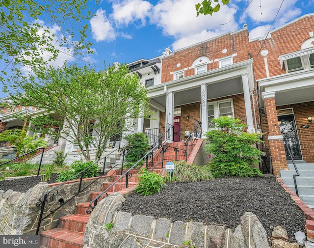 view of front of property featuring brick siding, stairs, and a porch