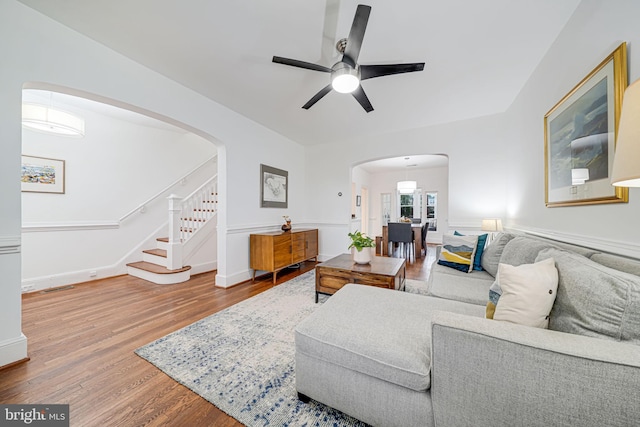 living room with arched walkways, ceiling fan, wood finished floors, and stairs