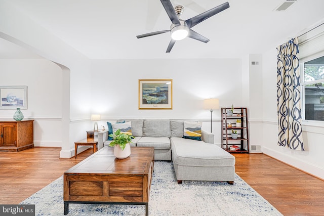 living room featuring wood finished floors, ceiling fan, baseboards, and arched walkways