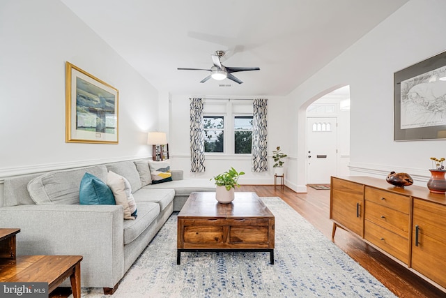 living area with arched walkways, ceiling fan, and wood finished floors