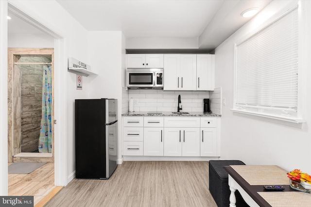1004 Philadelphia Ave, Ocean City, MD 21842 - kitchen with appliances with stainless steel finishes, light stone countertops, light wood finished floors, white cabinets, and decorative backsplash