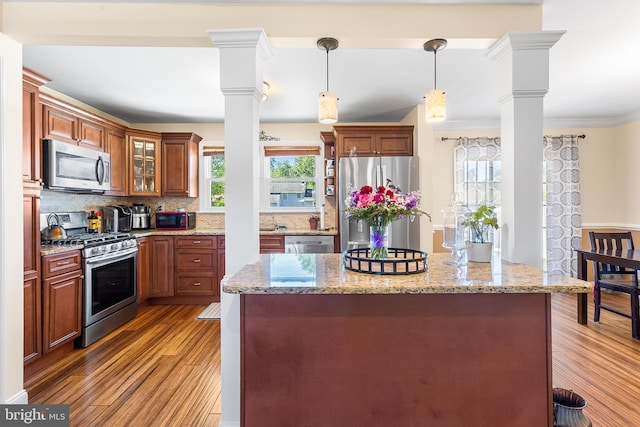 kitchen featuring stainless steel appliances, light wood finished floors, backsplash, pendant lighting, and crown molding
