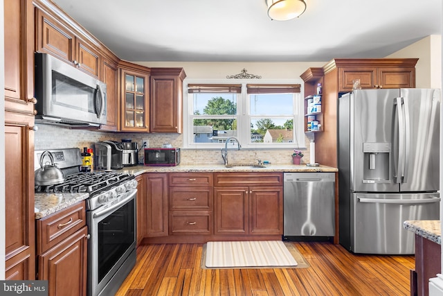 kitchen featuring stainless steel appliances, a sink, dark wood-style flooring, decorative backsplash, and light stone counters