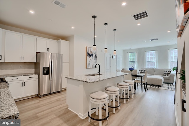kitchen with stainless steel fridge, a sink, light wood-type flooring, open floor plan, and white cabinets