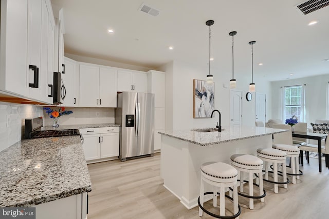 kitchen featuring stainless steel appliances, a sink, light wood-style flooring, white cabinets, and a kitchen breakfast bar