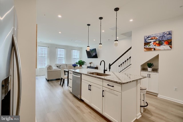 kitchen with appliances with stainless steel finishes, a sink, light wood-style flooring, white cabinetry, and light stone countertops