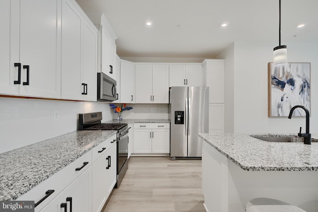 kitchen with stainless steel appliances, a sink, white cabinets, light stone countertops, and recessed lighting