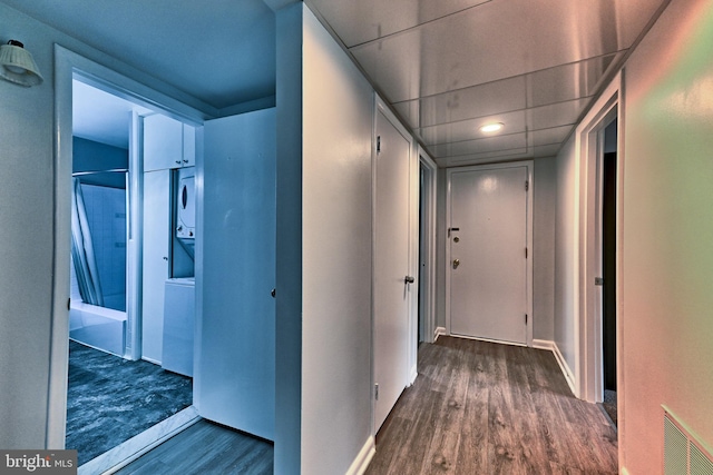 corridor featuring stacked washer / drying machine, wood finished floors, and baseboards