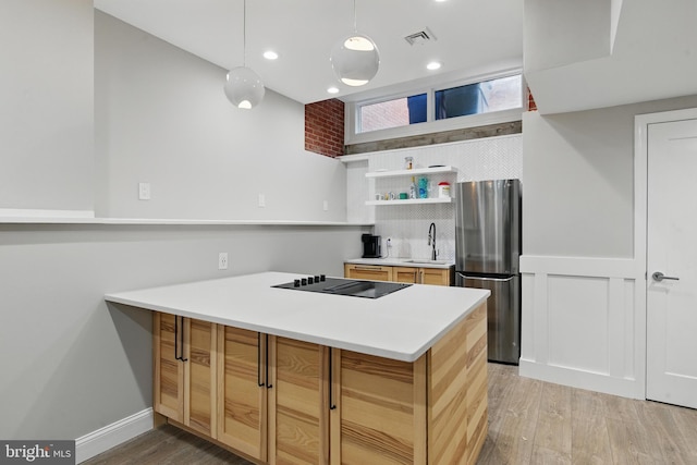 kitchen with freestanding refrigerator, black electric stovetop, a peninsula, a sink, and light wood-style flooring
