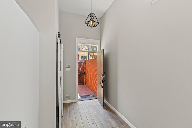 hall featuring wood finished floors, baseboards, and a barn door