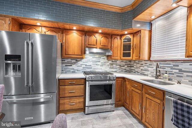 kitchen with appliances with stainless steel finishes, under cabinet range hood, a sink, brown cabinetry, and light countertops
