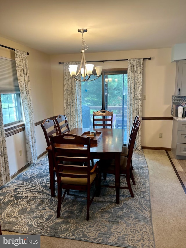 dining area featuring a chandelier, light carpet, and baseboards