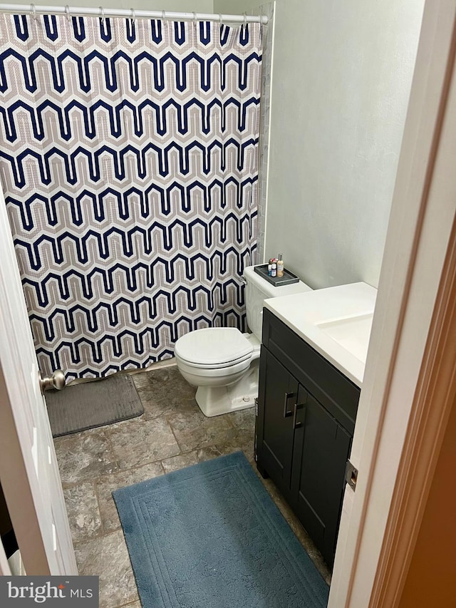 bathroom with stone tile flooring, a tile shower, toilet, and vanity