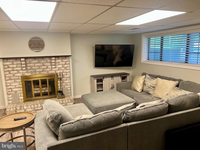 living room featuring wood finished floors, a paneled ceiling, and a brick fireplace