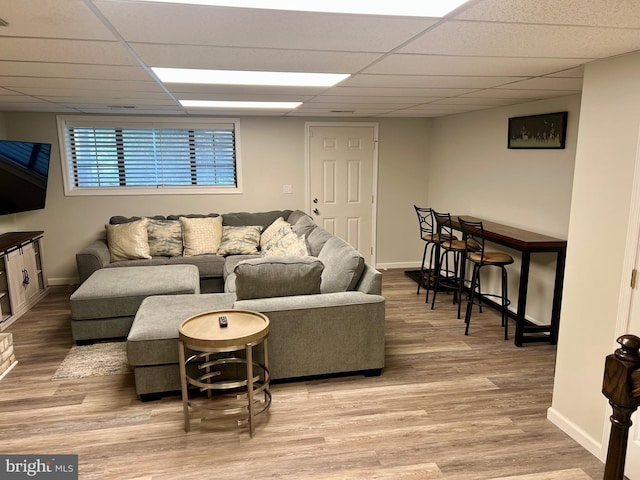 living area featuring a drop ceiling, light wood finished floors, and baseboards