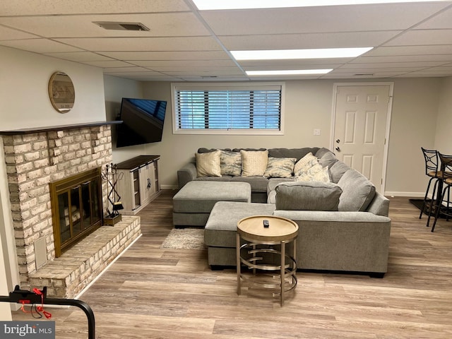 living area featuring a paneled ceiling, wood finished floors, baseboards, and a brick fireplace