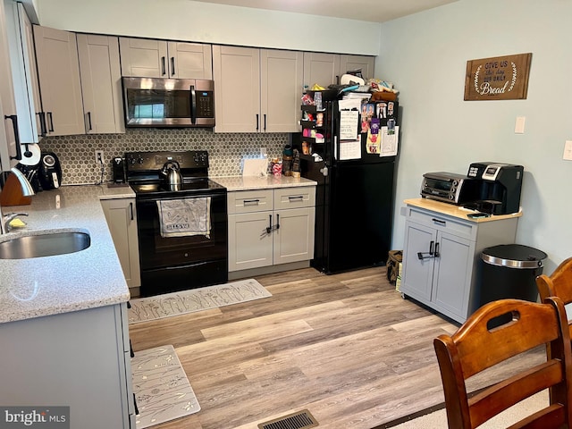 kitchen with black appliances, a sink, light wood-style flooring, backsplash, and gray cabinets