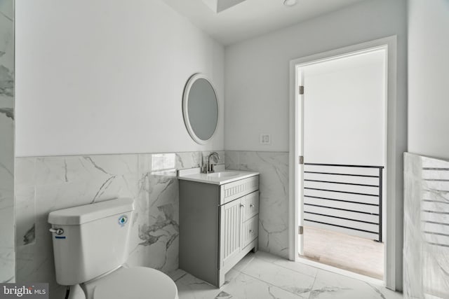 bathroom with marble look tiles, tile walls, a wainscoted wall, toilet, and vanity