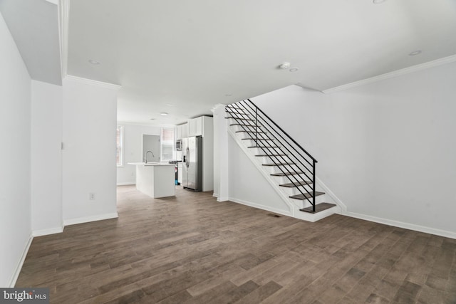 unfurnished living room with ornamental molding, dark wood-style flooring, stairway, baseboards, and a sink