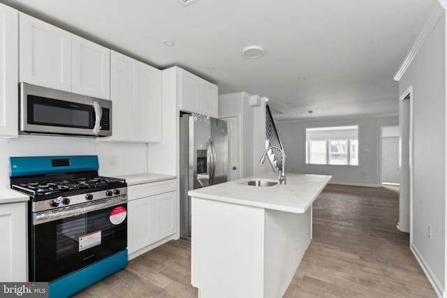 kitchen with appliances with stainless steel finishes, a sink, open floor plan, light wood-style flooring, and white cabinetry