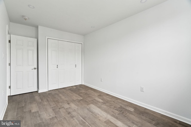 unfurnished bedroom with wood finished floors, baseboards, and a closet