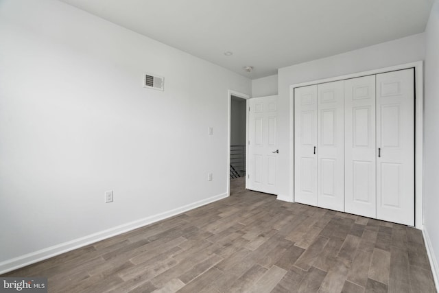 unfurnished bedroom featuring wood finished floors, baseboards, and a closet