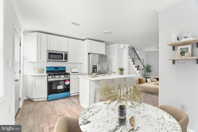 kitchen featuring stainless steel appliances, light wood-style floors, light countertops, white cabinets, and crown molding