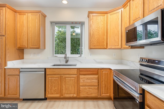 kitchen with stainless steel appliances, a sink, light wood-type flooring, recessed lighting, and light stone countertops