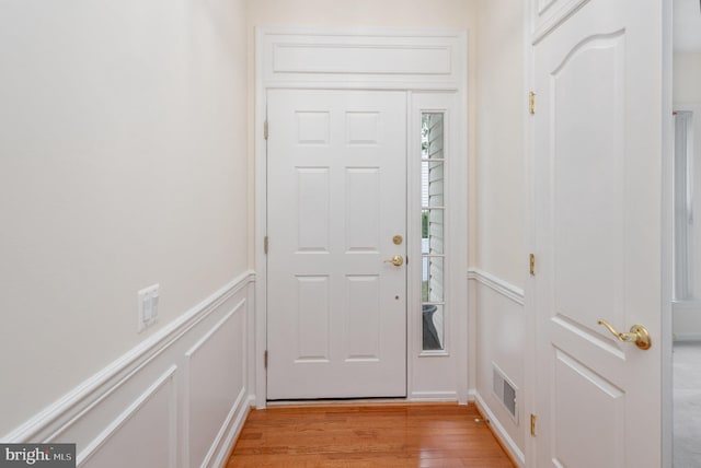 foyer with light wood-style floors, a decorative wall, and a wainscoted wall