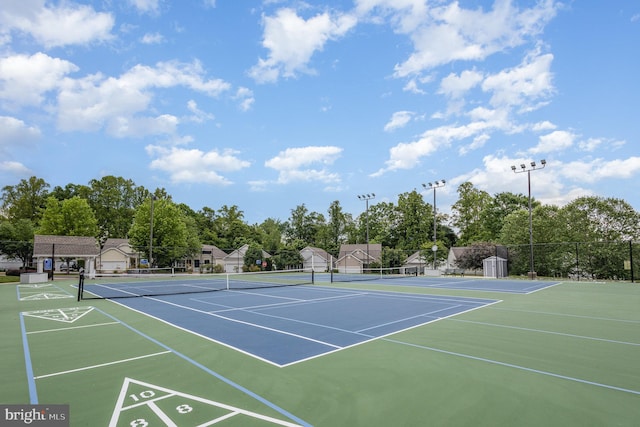 view of tennis court with community basketball court, fence, and view of scattered trees