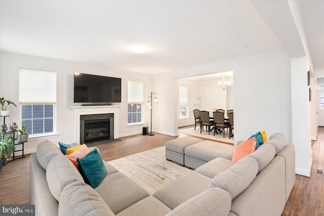living room with a chandelier, wood finished floors, baseboards, and a fireplace with flush hearth