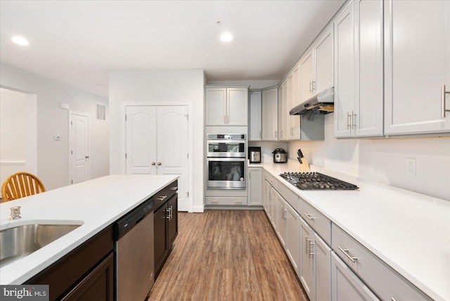 kitchen with appliances with stainless steel finishes, under cabinet range hood, light countertops, wood finished floors, and recessed lighting