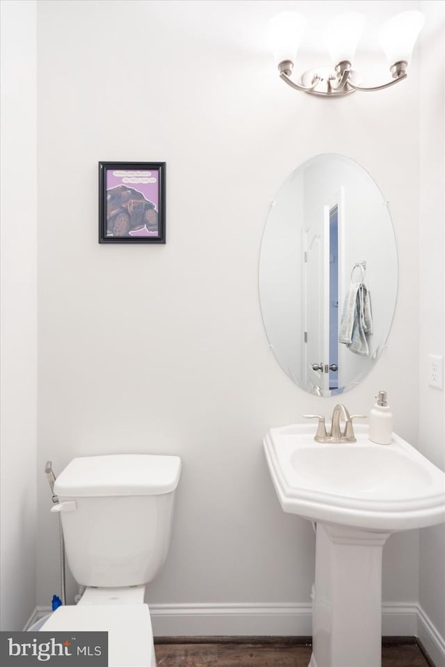 half bath with toilet, baseboards, and wood finished floors